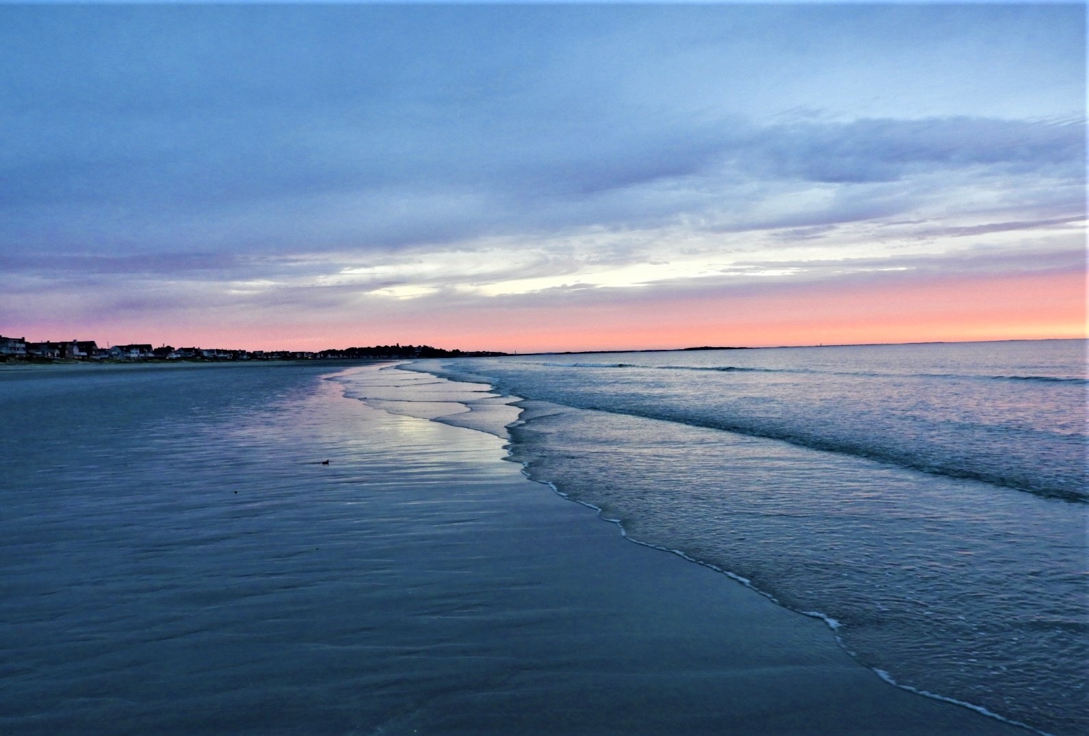 Calm beach at dusk with soft waves reflecting a blue and pink sky